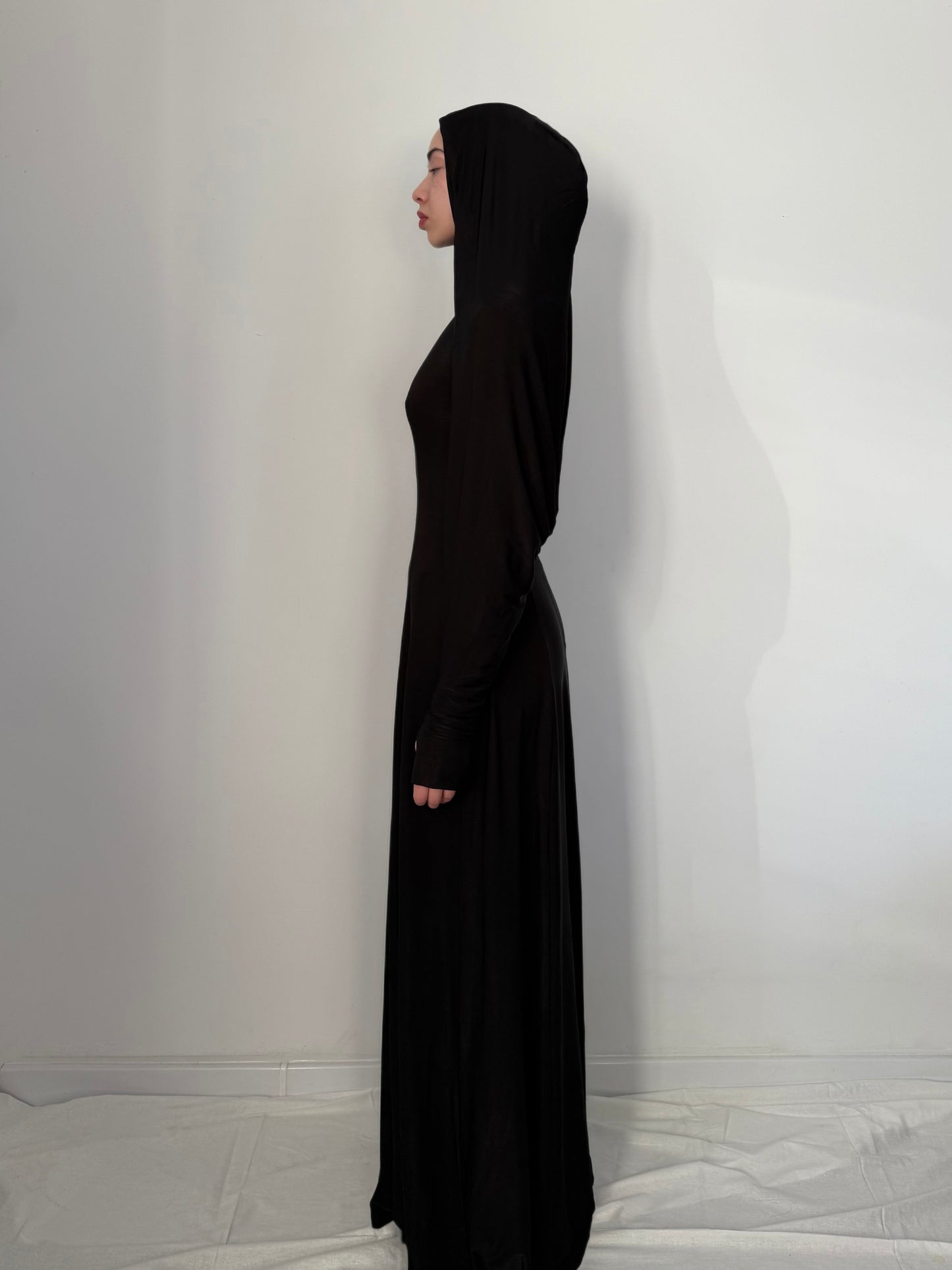 Person wearing a long black dress with a hood against a white background