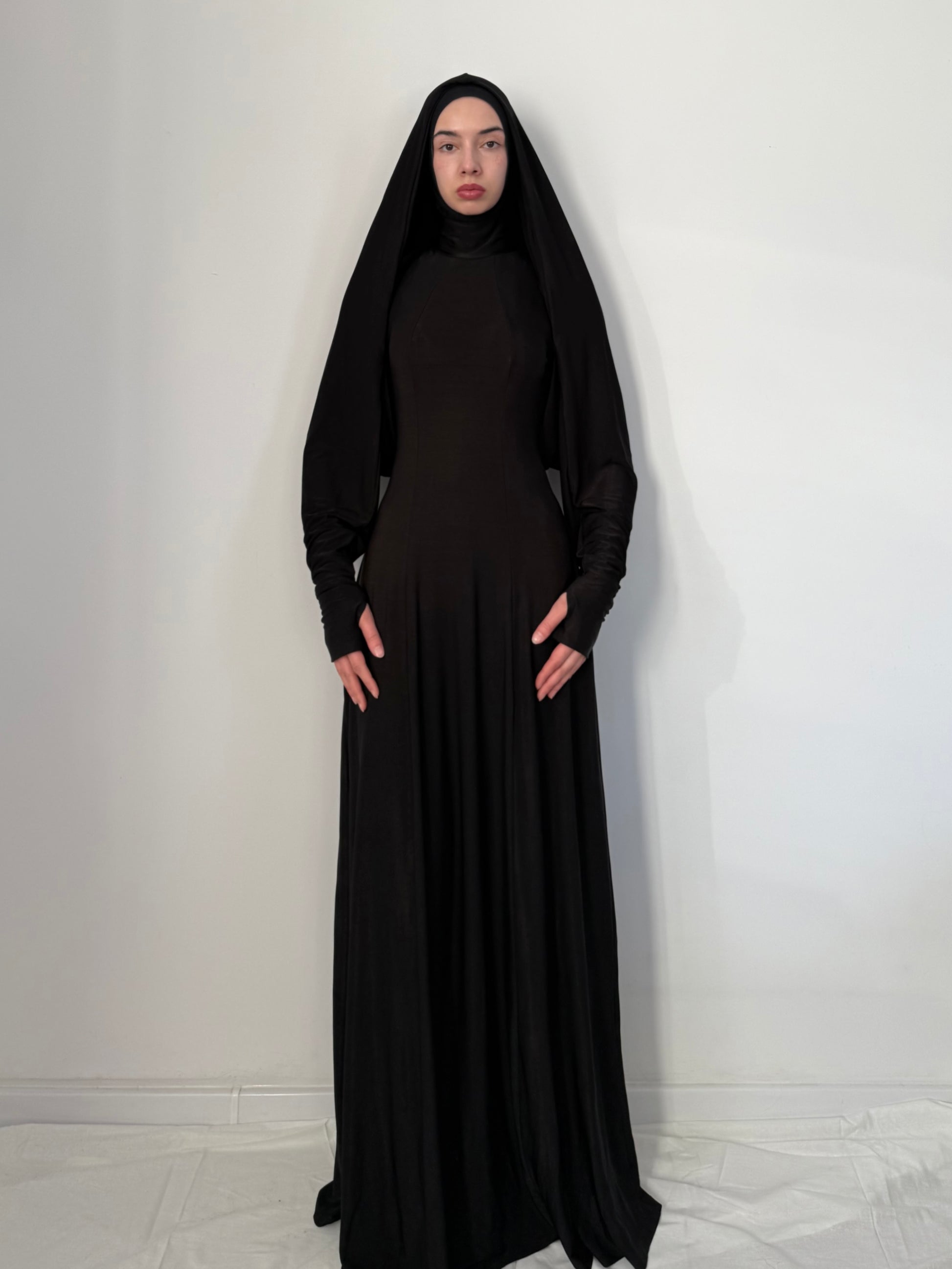 Person wearing a long black dress with a hood against a white background