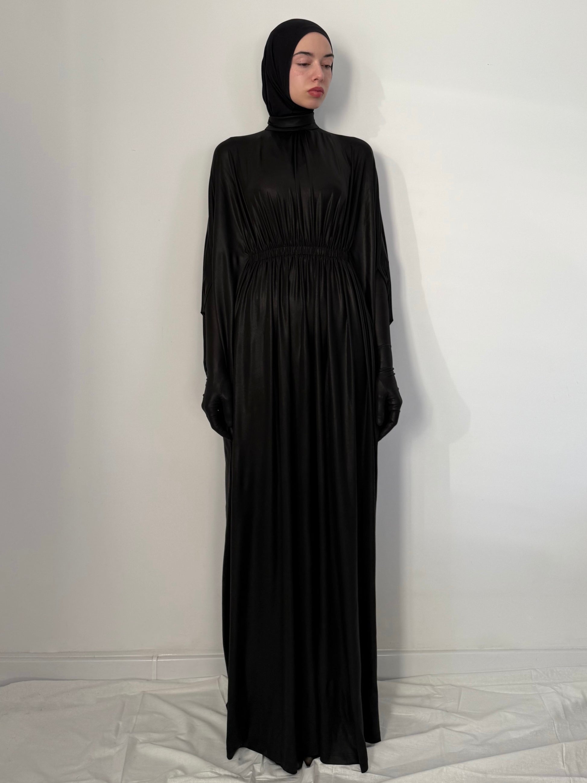 Woman wearing a black abaya and hijab against a white background