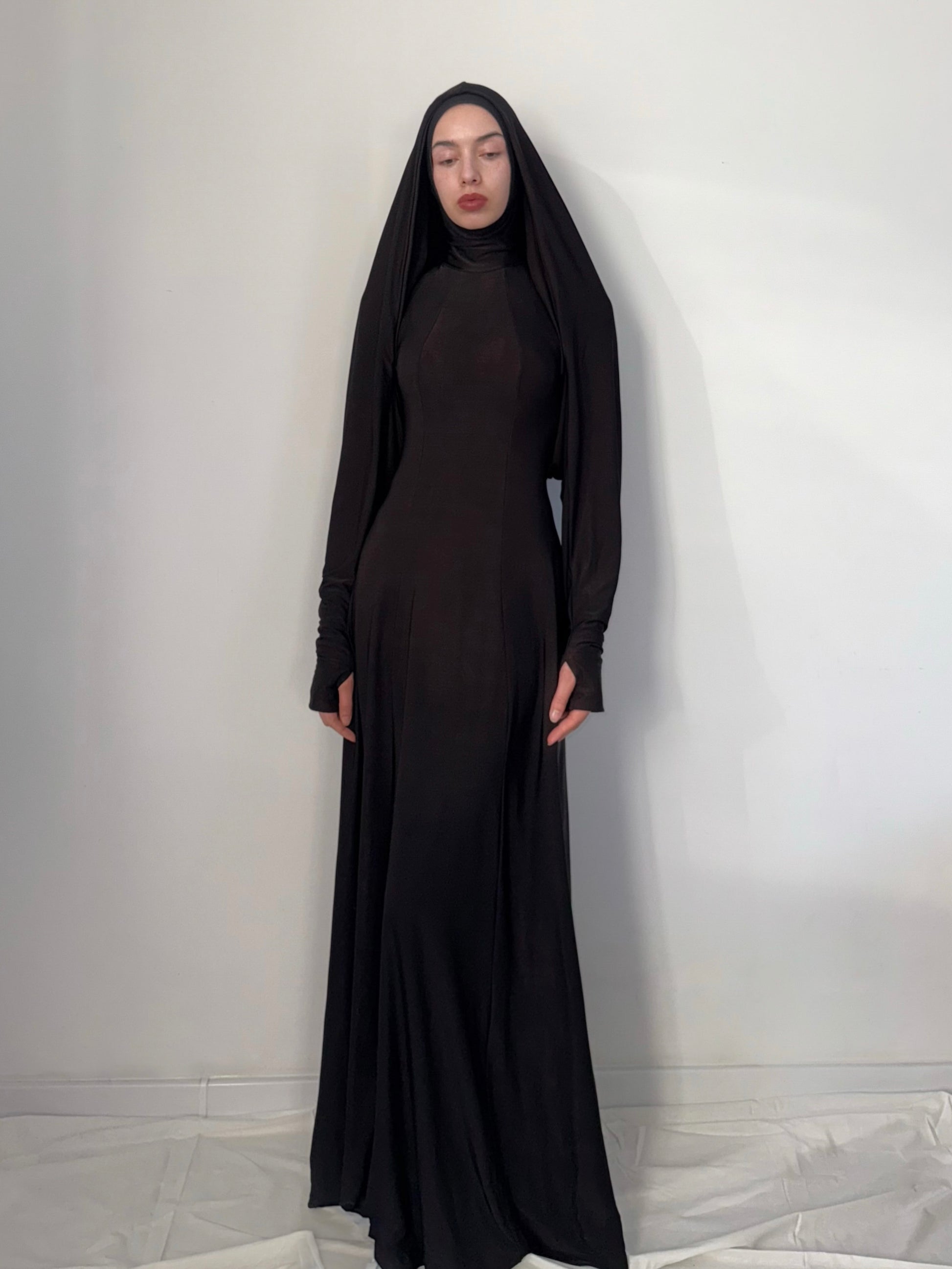 Person wearing a long black dress with a hood against a white background